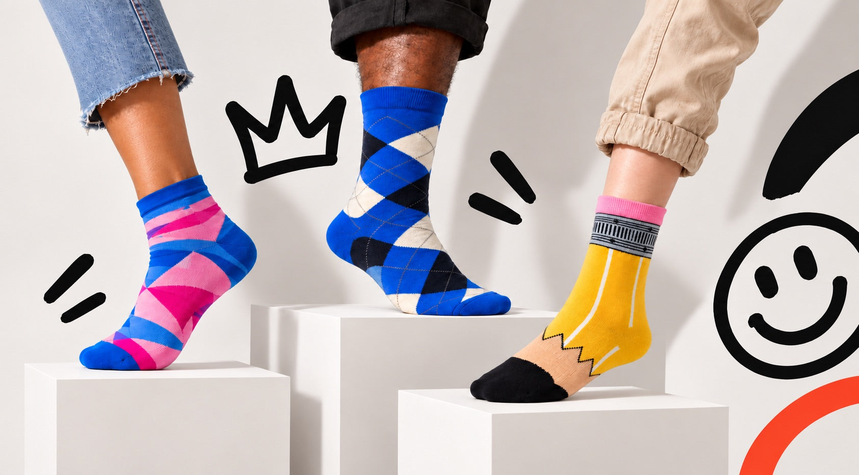 Three colorful Motsu socks on white plinths against a hand-drawn crown and smiley backdrop